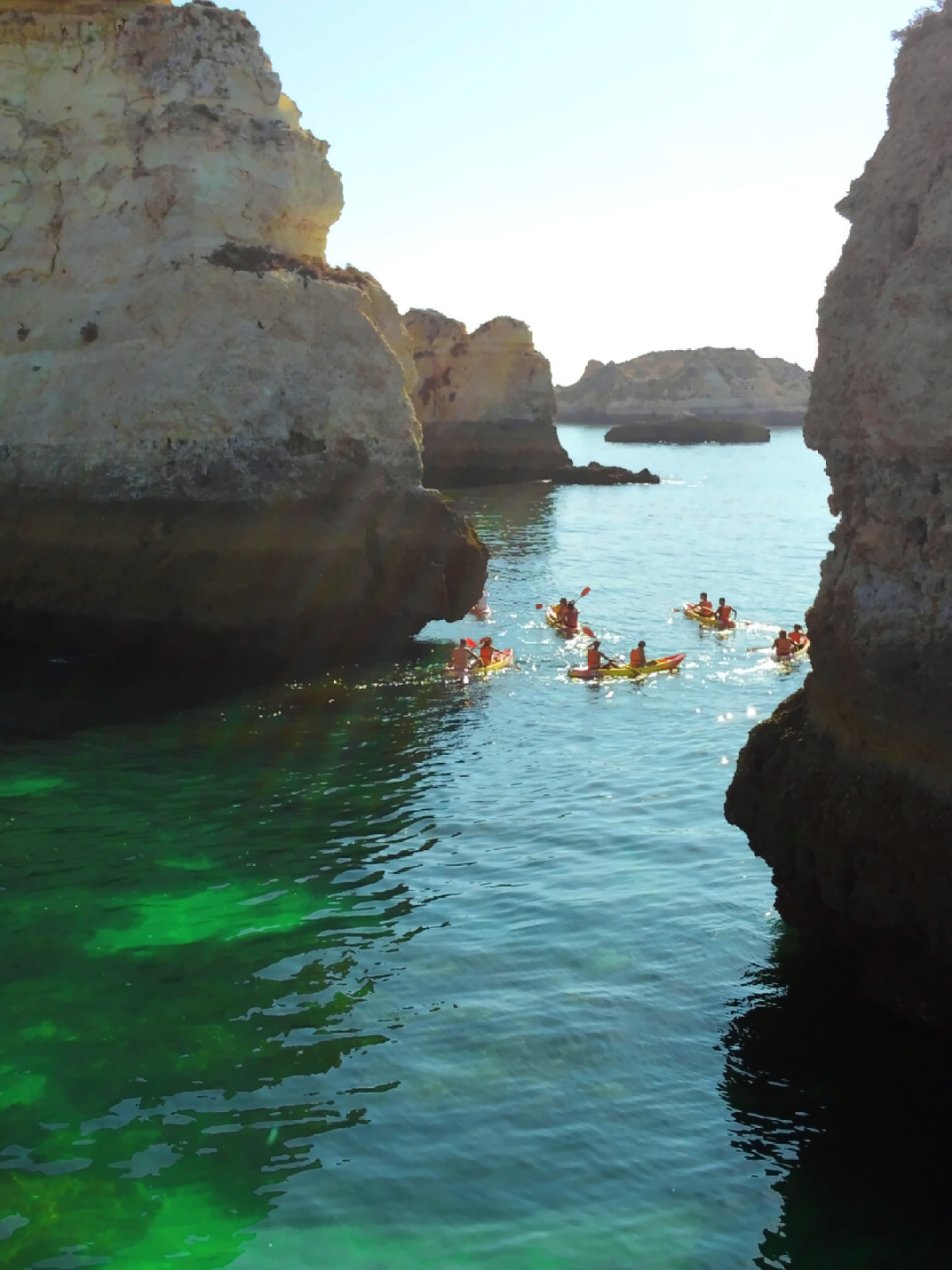 Kayakers exploring between large coastal cliffs on a sunny day.