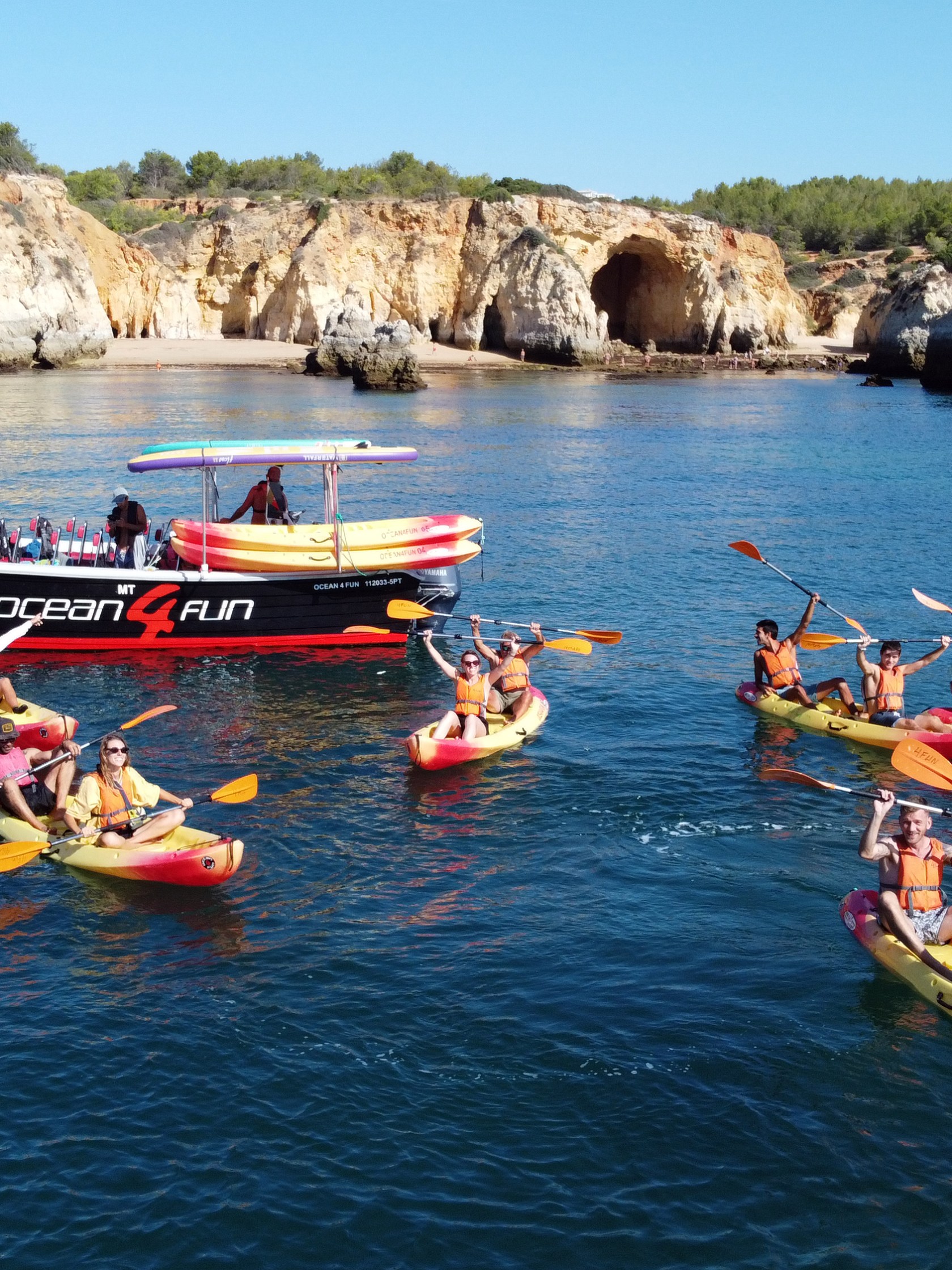 Kayakers paddling near a tour boat in a rocky coastal area.
