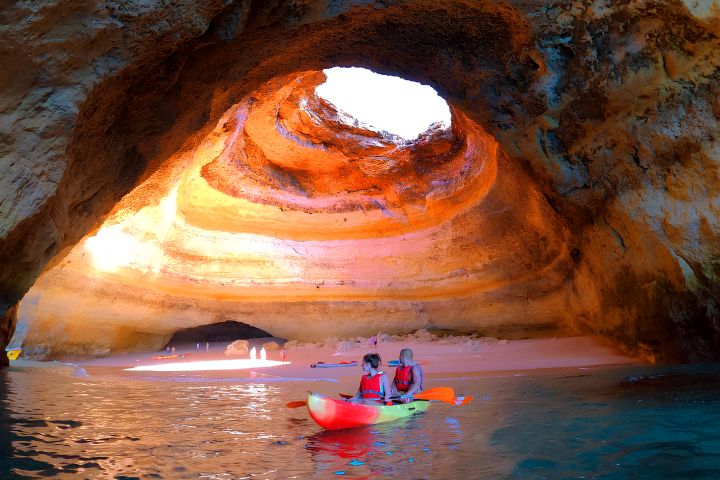 Two people kayaking inside a sunlit coastal cave.