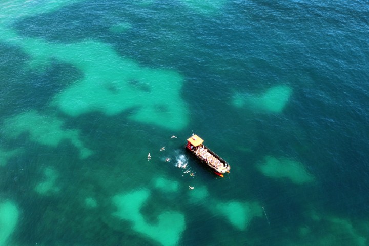 Aerial view of a boat in clear blue-green water with swimmers nearby.