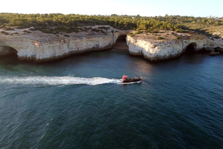 Boat in ocean passing rugged cliffs with greenery on top.