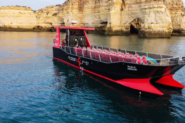 Tour boat with red and black design near rocky cliffs on calm water.