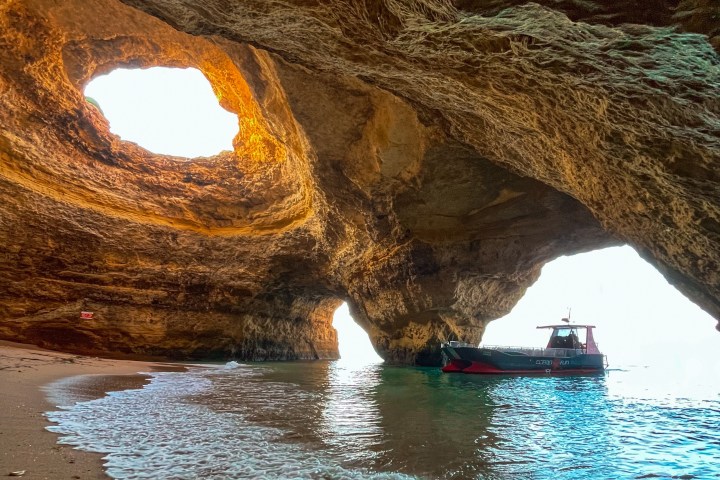 Cave with sunlight through ceiling, boat on water inside.