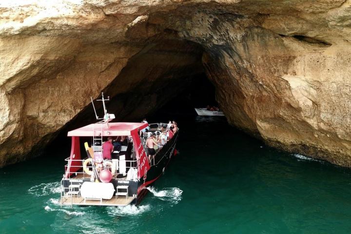 Boat entering a large cave on a rocky shoreline.