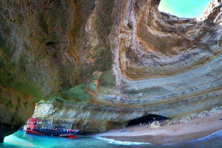 Tourists in a boat inside a large ocean cave with a sandy beach.