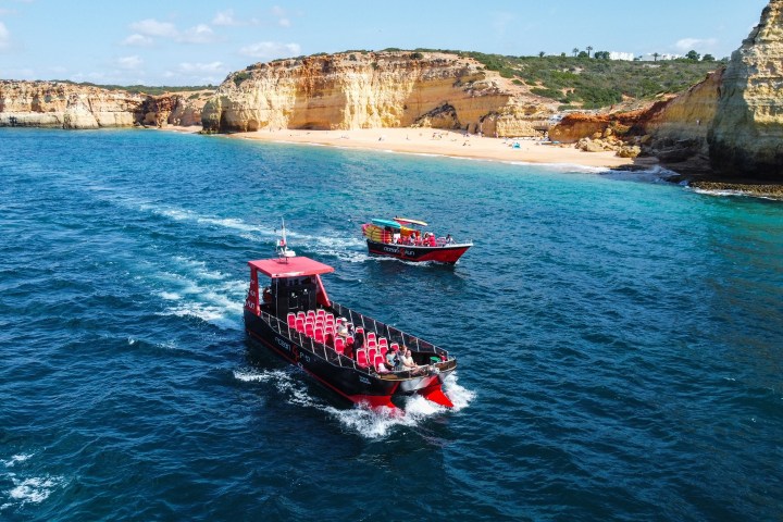 Two boats on a blue ocean near a rocky coastline and sandy beach.