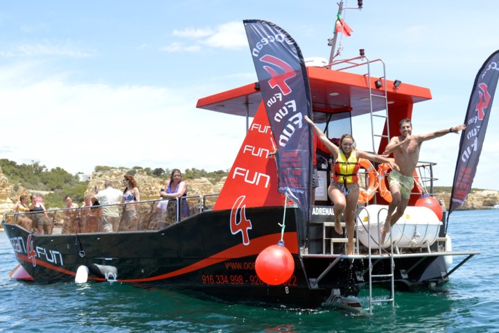 People on a boat with red details, some preparing to swim, on a sunny day.