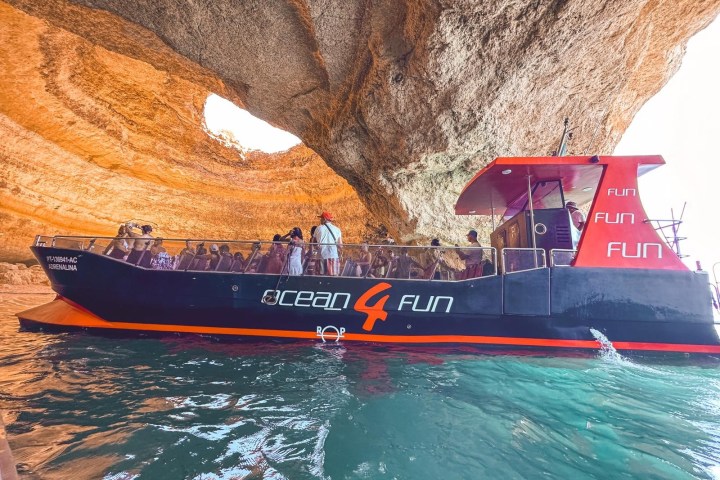 Tour boat with people in a cave with sunlight through openings.