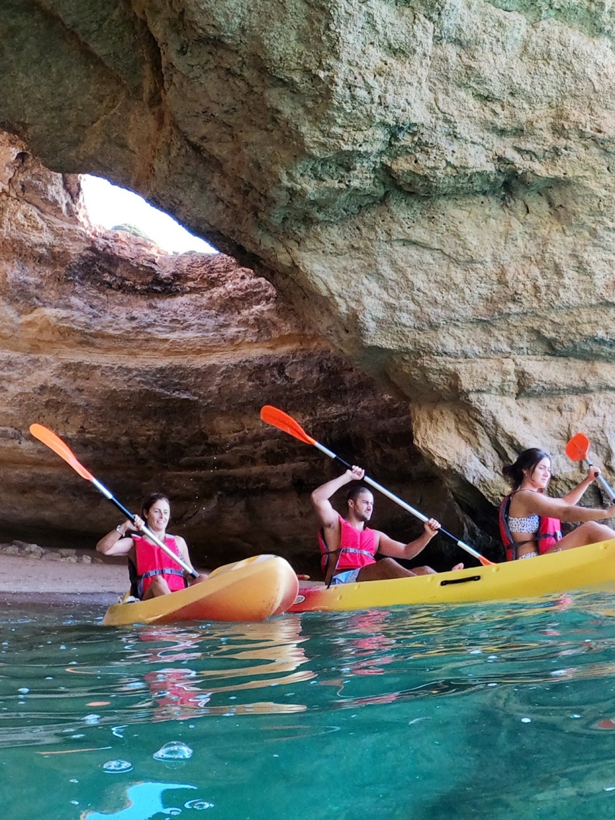 Three people kayaking near a rocky cave.