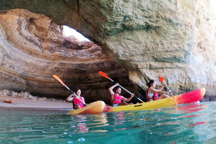 Three people kayaking near a rocky cave.