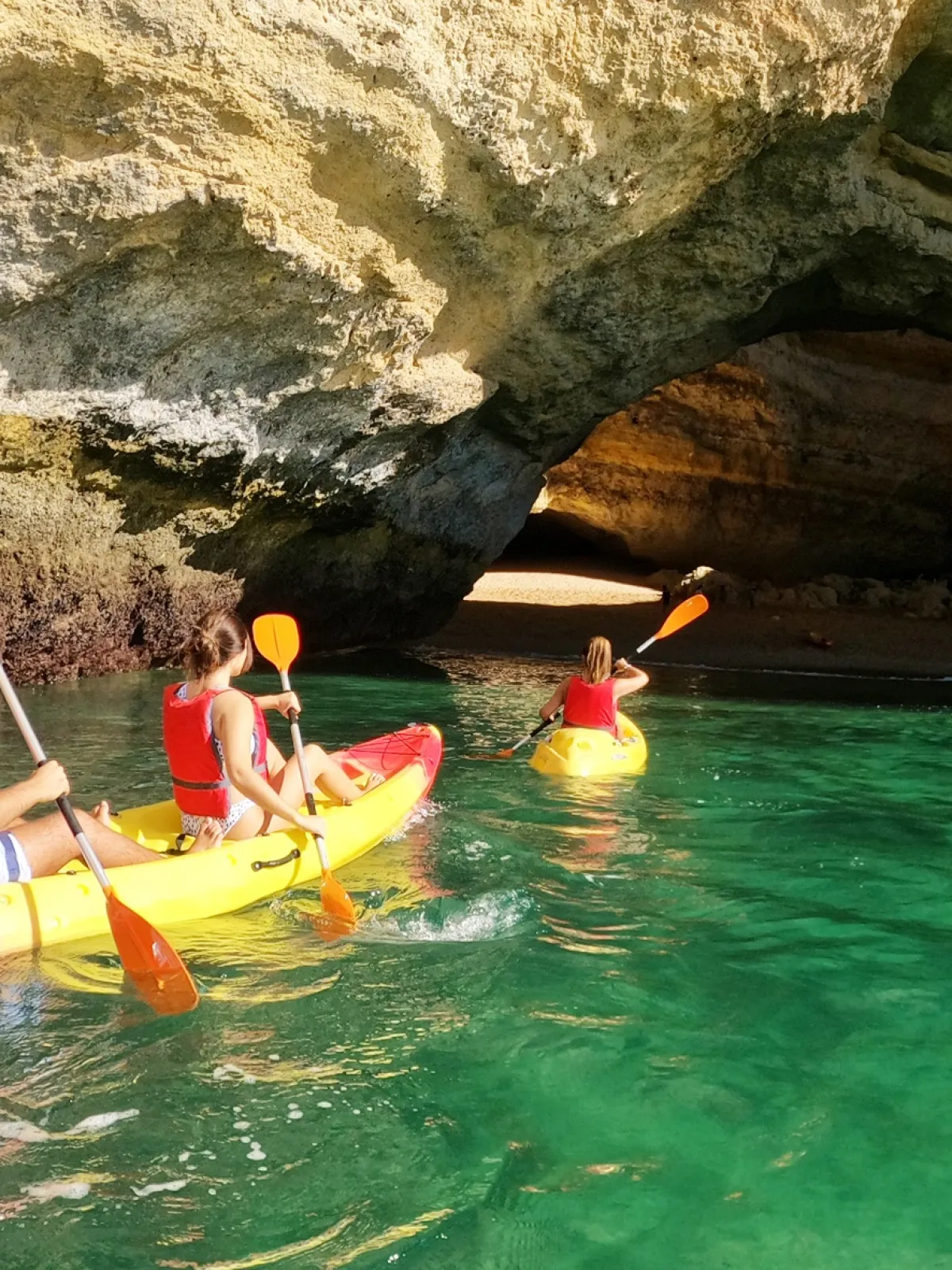 Three people kayaking towards a cave in clear green water.