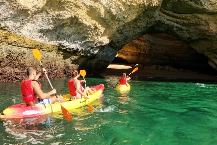 Three people kayaking towards a cave in clear green water.