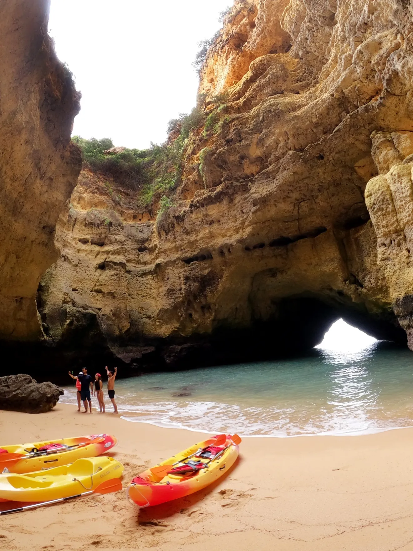 People with kayaks on a sandy beach inside a large cave.