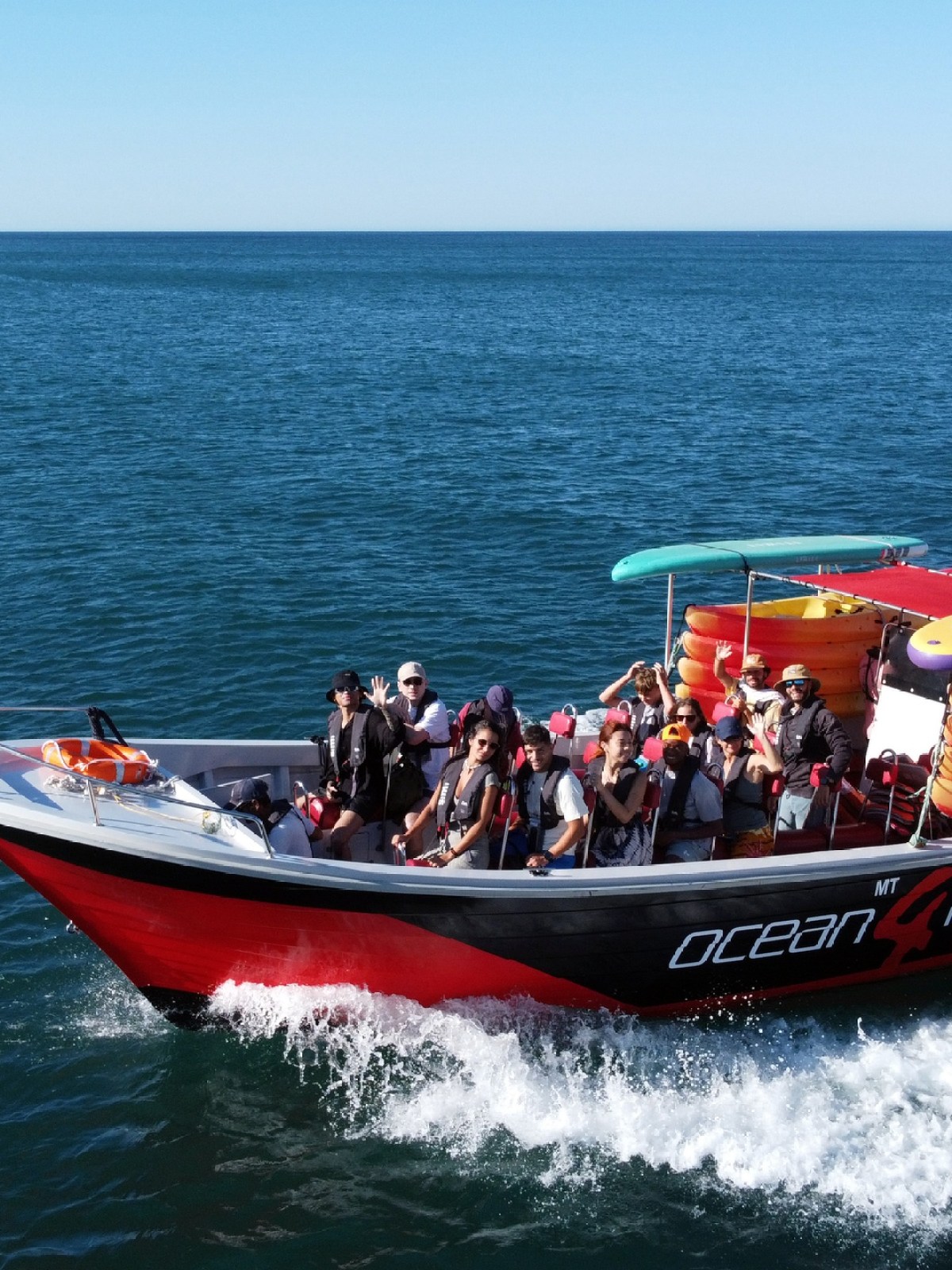 A red boat with passengers cruising on a vast blue ocean under clear skies.