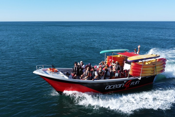 A red boat with passengers cruising on a vast blue ocean under clear skies.