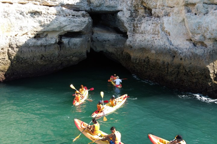 Group kayaking near a rocky cave entrance on calm water.