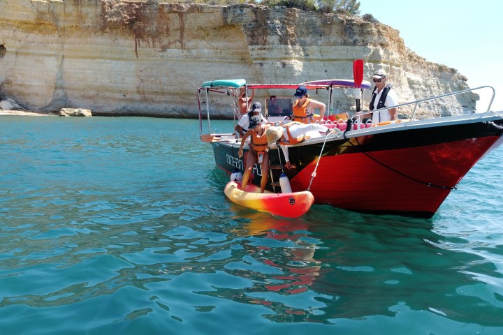 People on a red boat near a cliffside with clear blue water.