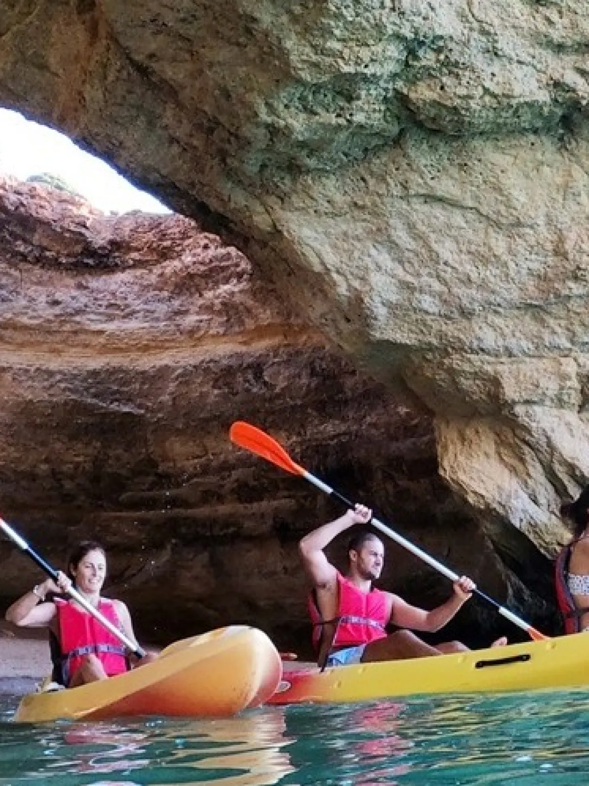Three people kayaking in a cave with kayaks and oars.