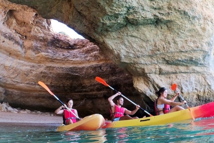 Three people kayaking in a cave with kayaks and oars.