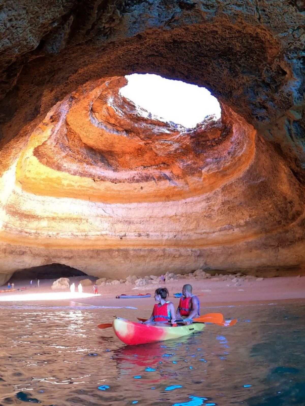 Two people kayaking in a cave with a large opening overhead.