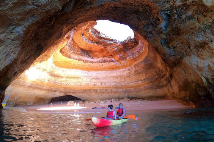 Two people kayaking in a cave with a large opening overhead.