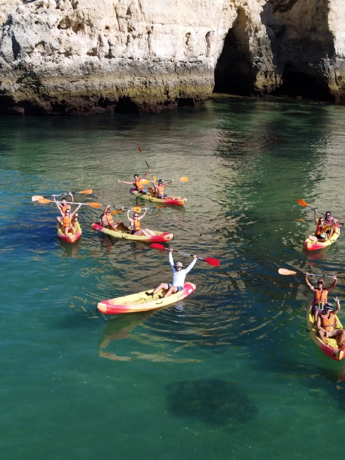 Group kayaking near rocky cliffs in clear blue water.