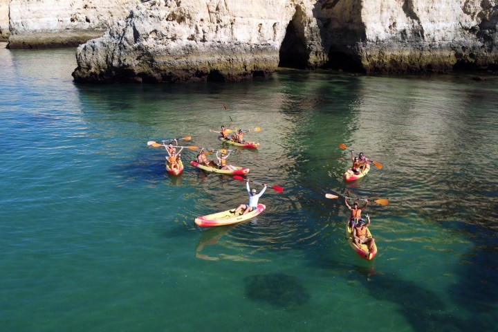 Group kayaking near rocky cliffs in clear blue water.