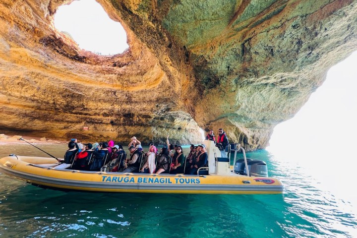 People on a yellow boat tour inside a sea cave with a large opening above.