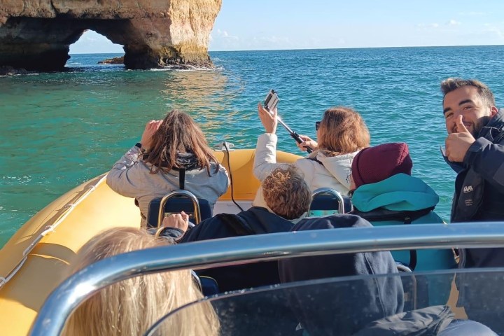 People on a boat near a rocky coastal cliff under a clear blue sky.