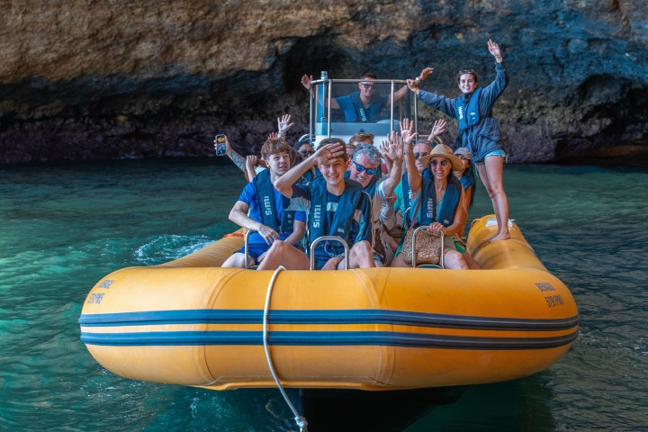 Group on yellow inflatable boat in cave, waving and smiling.