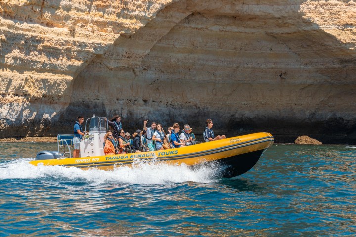 Yellow boat with people in life jackets near rocky cliffs on the water.