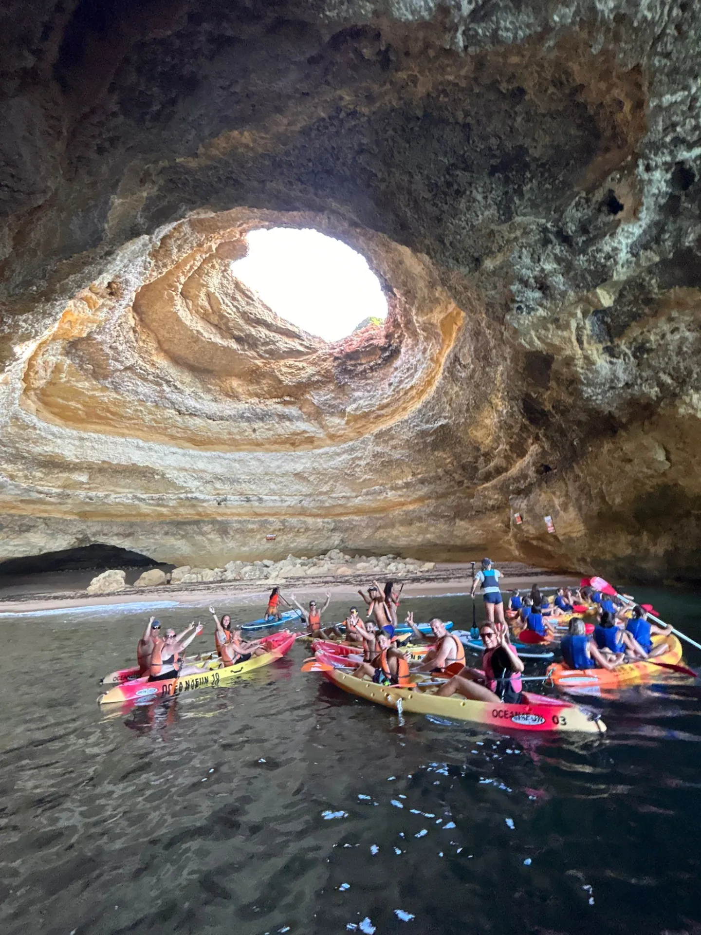 People kayaking inside a large cave with a circular opening above.