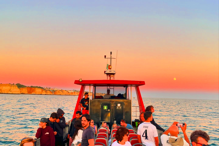 People on a boat enjoying a sunset with a clear sky and distant cliffs.