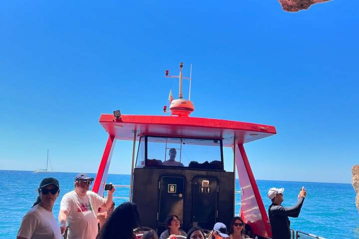 People on a boat under a rocky alcove with a clear blue sky.