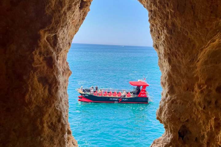 View of red boat on sea through rocky cave opening.