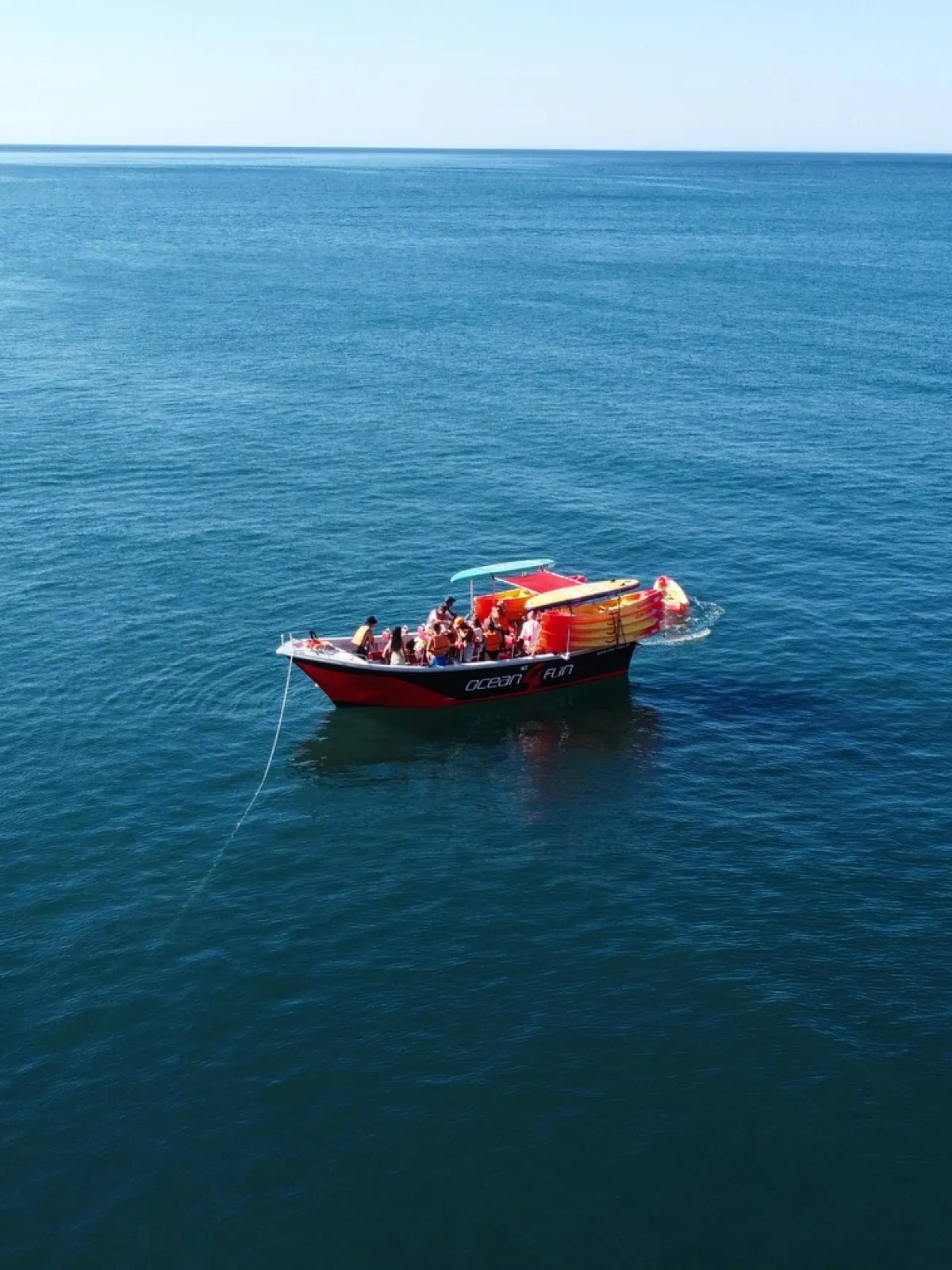 Small red boat with people anchored in calm, open sea.