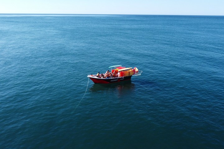Small red boat with people anchored in calm, open sea.