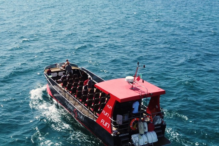 Speedboat with red canopy cruising on open sea under clear sky.