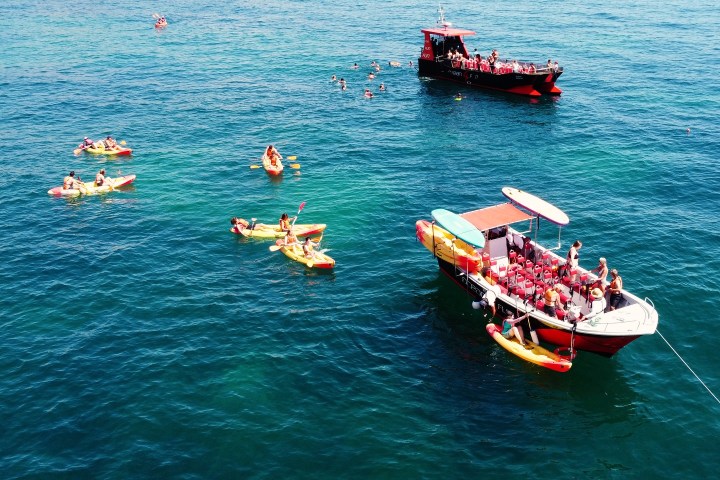 Boats and kayakers on a sunny, clear blue sea.