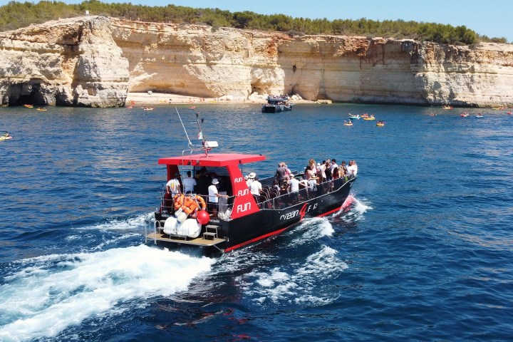Tour boat with passengers near rocky coast and clear blue sea.