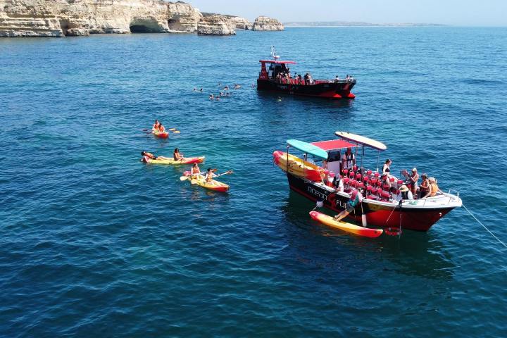 Boats and kayaks on clear blue sea near rocky shore under bright sky.