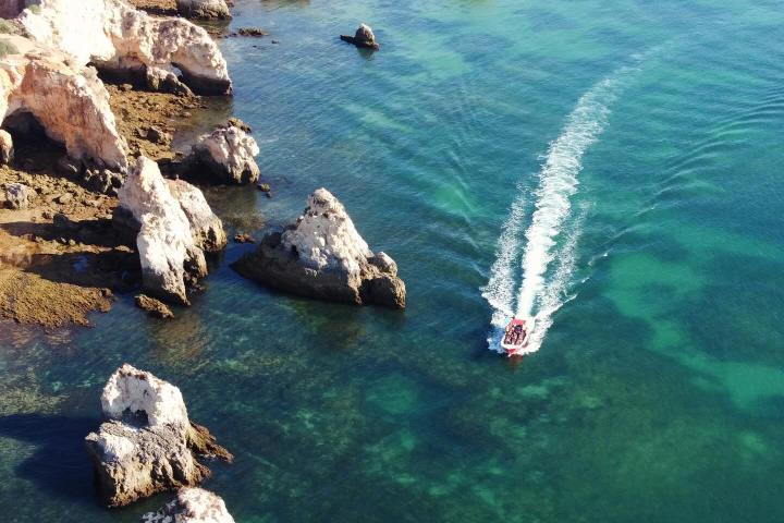 Boat navigates clear turquoise water near rocky coastline.