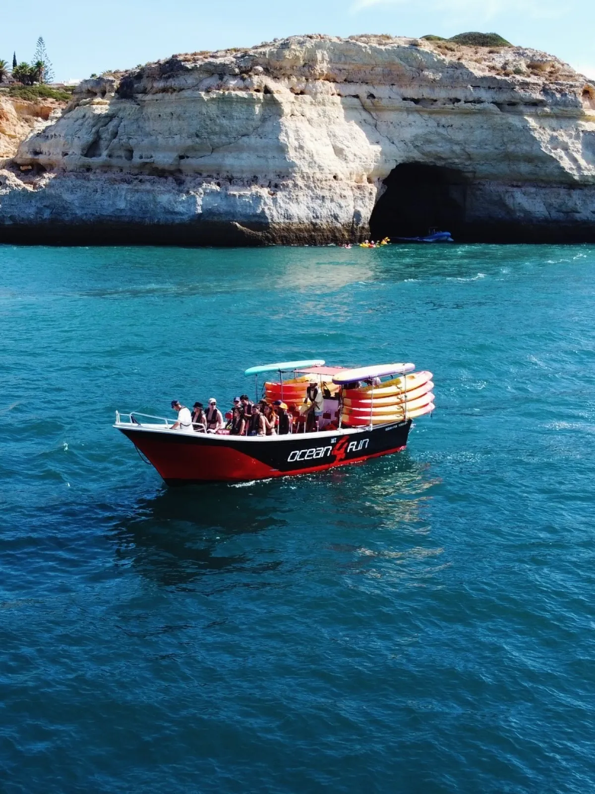 Boat with people in ocean near rocky cliff and cave.