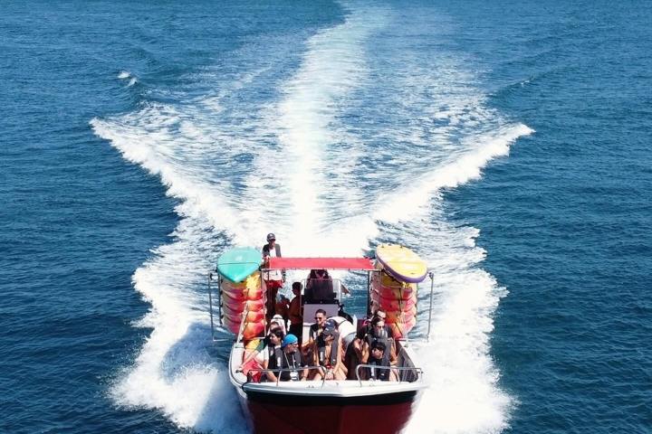 Red boat with passengers cruising on blue water leaving a white wake.