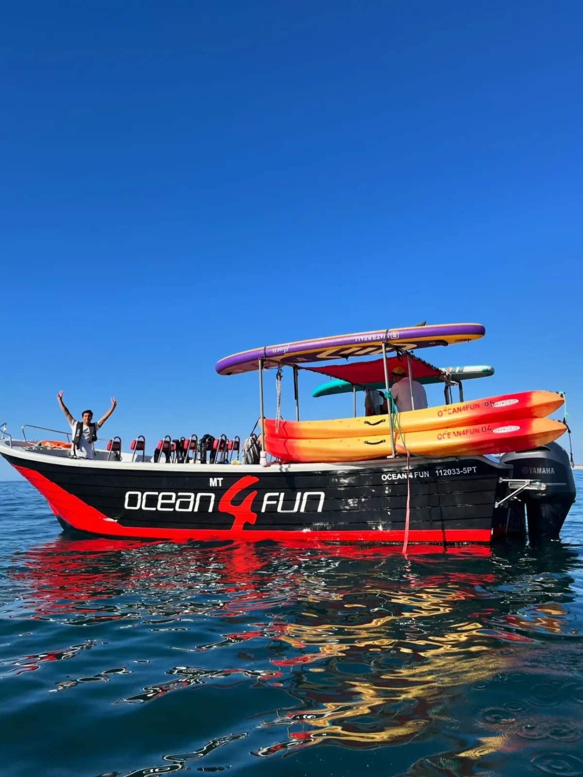 Boat with kayaks and life jackets on calm water, person cheering on deck.