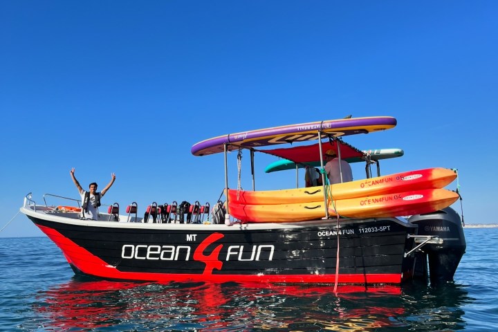 Boat with kayaks and life jackets on calm water, person cheering on deck.