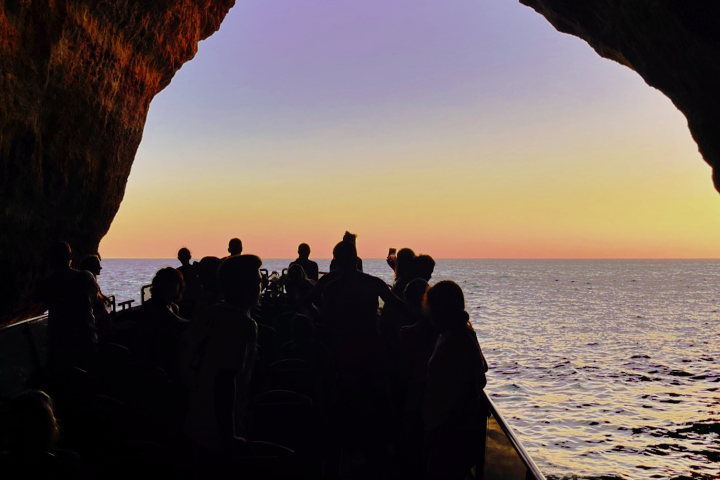 Silhouetted people in a cave with ocean and sunset view.